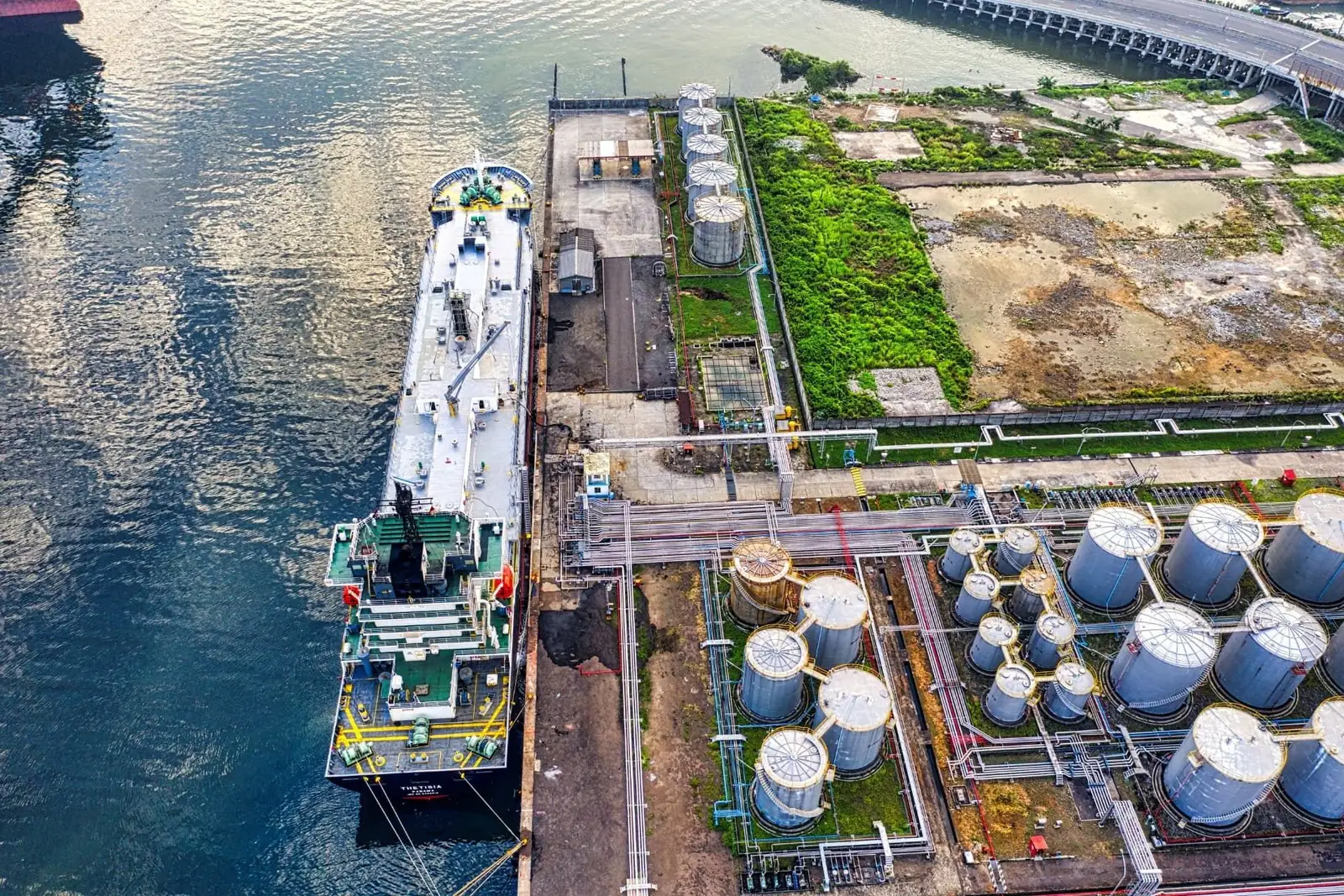Aerial view of an oil and gas marine terminal with storage tanks, pipework and a berthed vessel