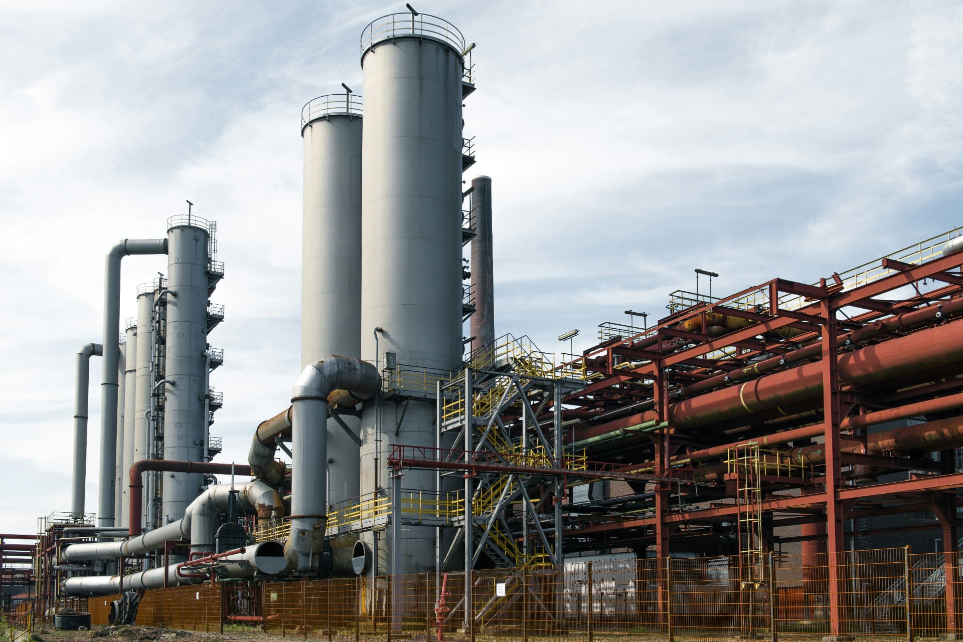 Ageing industrial process facility with tall vessels, pipework and painted structural steelwork