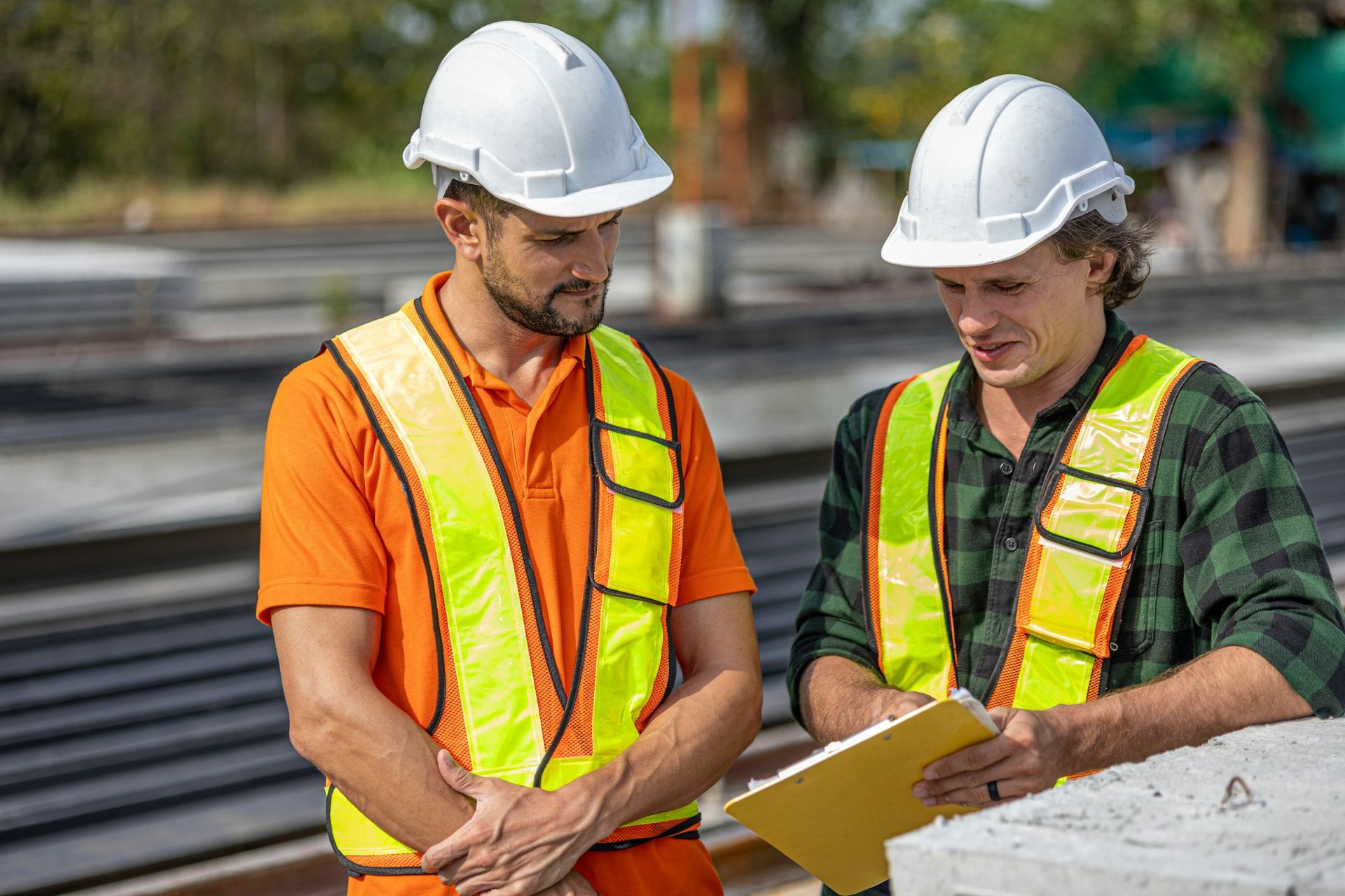 Two engineers in hard hats and high-visibility vests reviewing project information on site