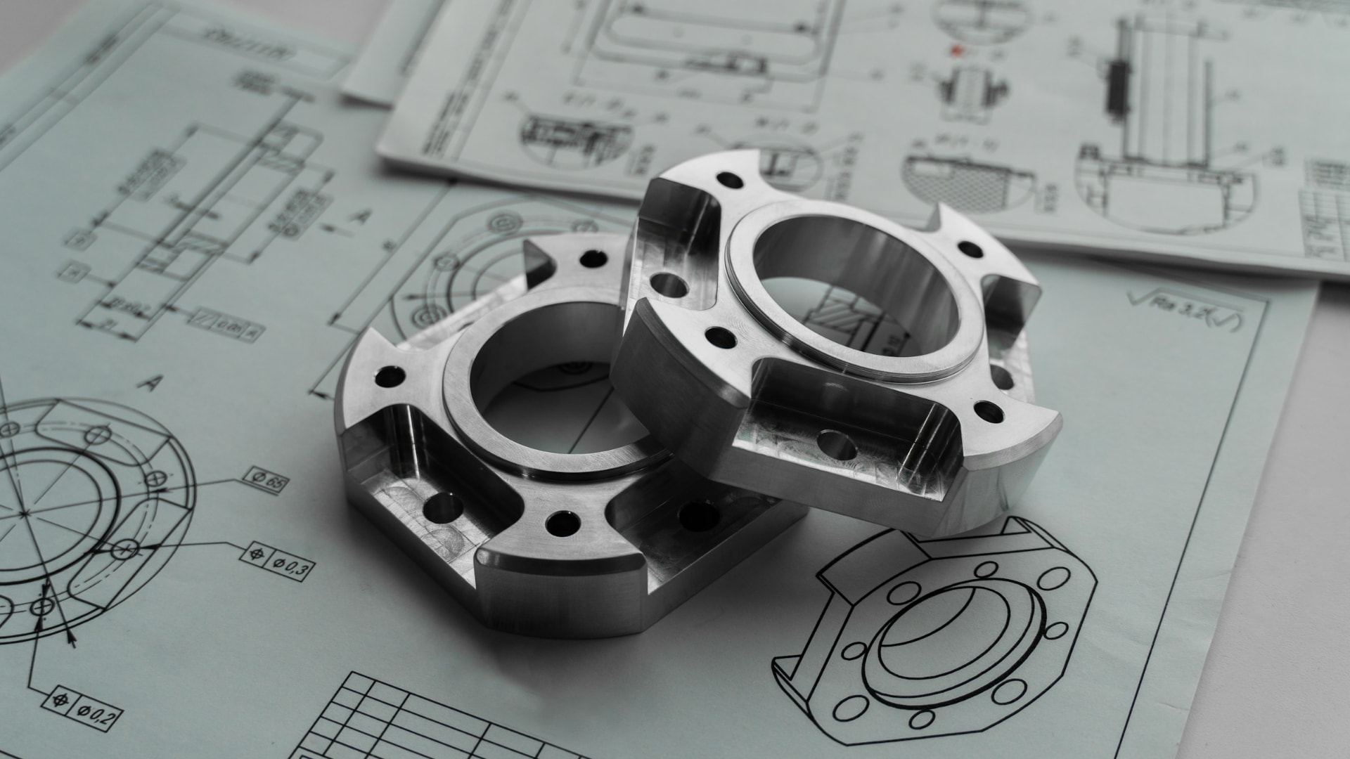 Machined metal components resting on technical engineering drawings